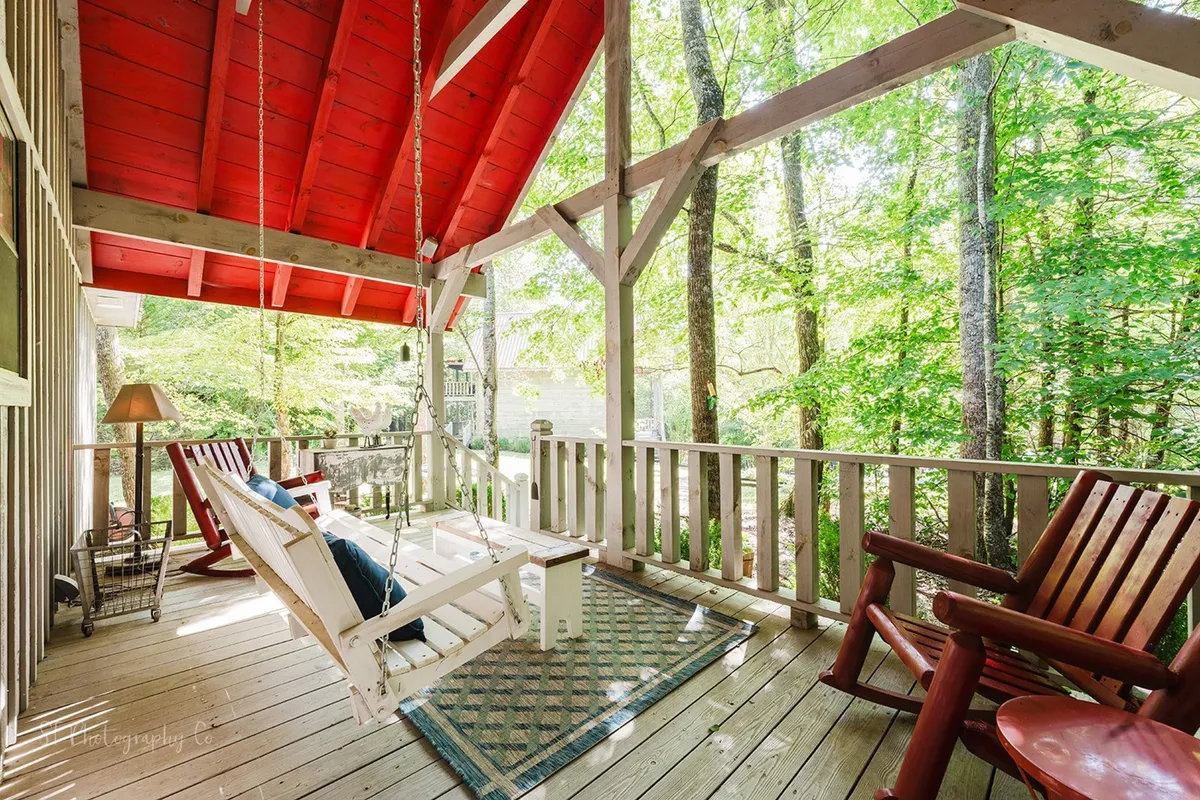 A tranquil porch scene with a swing chair, red roof, and verdant trees all around. The flooring and seating make it ideal for reading, stargazing, or simply savoring the fresh mountain air.