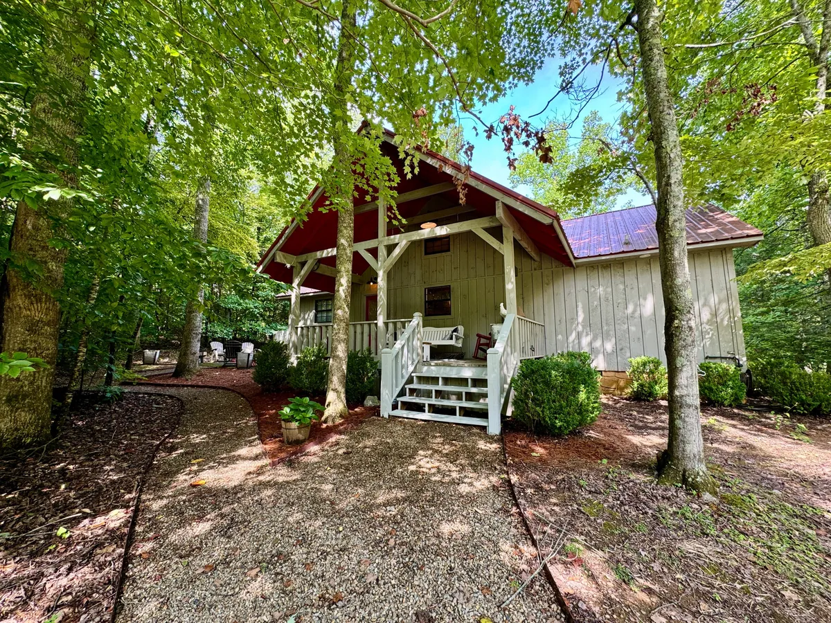 A view of the front porch, gravel pathway, and surrounding trees. The outdoor setting feels serene and ideal for both people and pets to unwind after a day of exploring trails. The porch invites relaxation after an adventure, while the pathway hints at easy access to walking routes.
