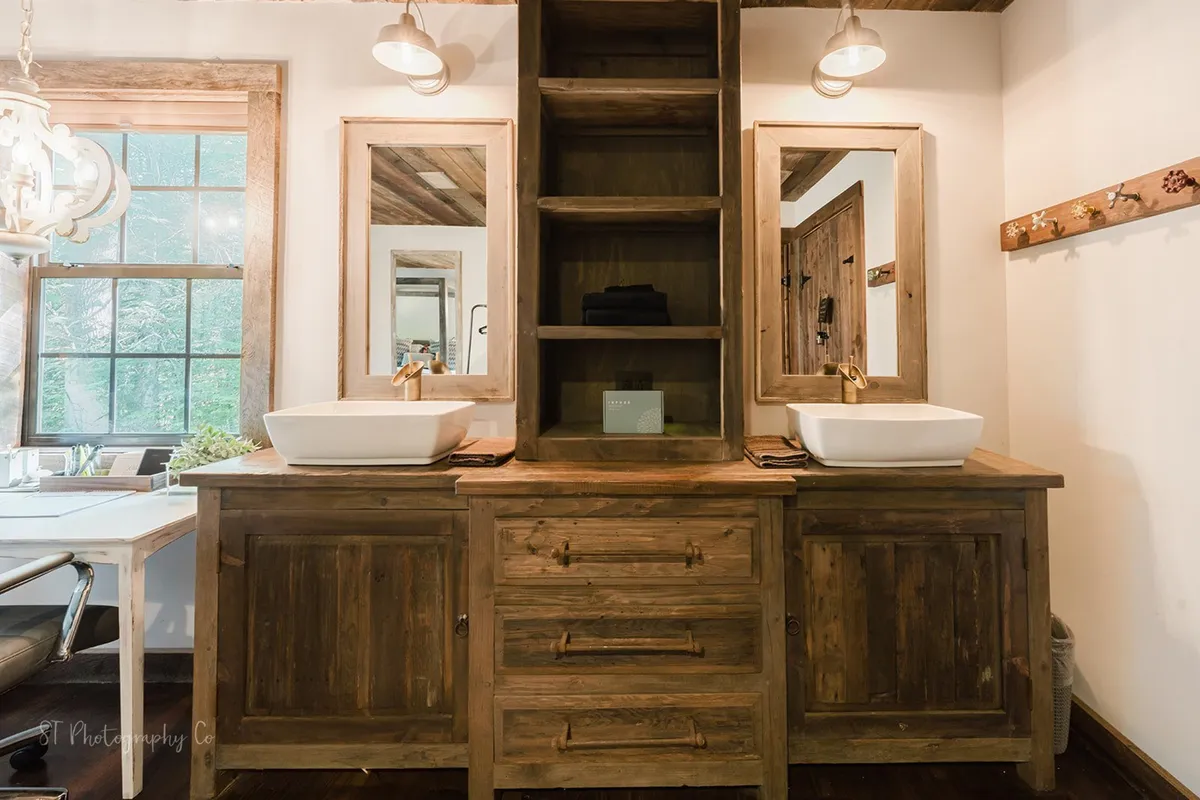 A cozy bathroom scene with a wooden vanity, dual mirrors, sinks, and an open shelving unit, creating an inviting space for self-care and relaxation.