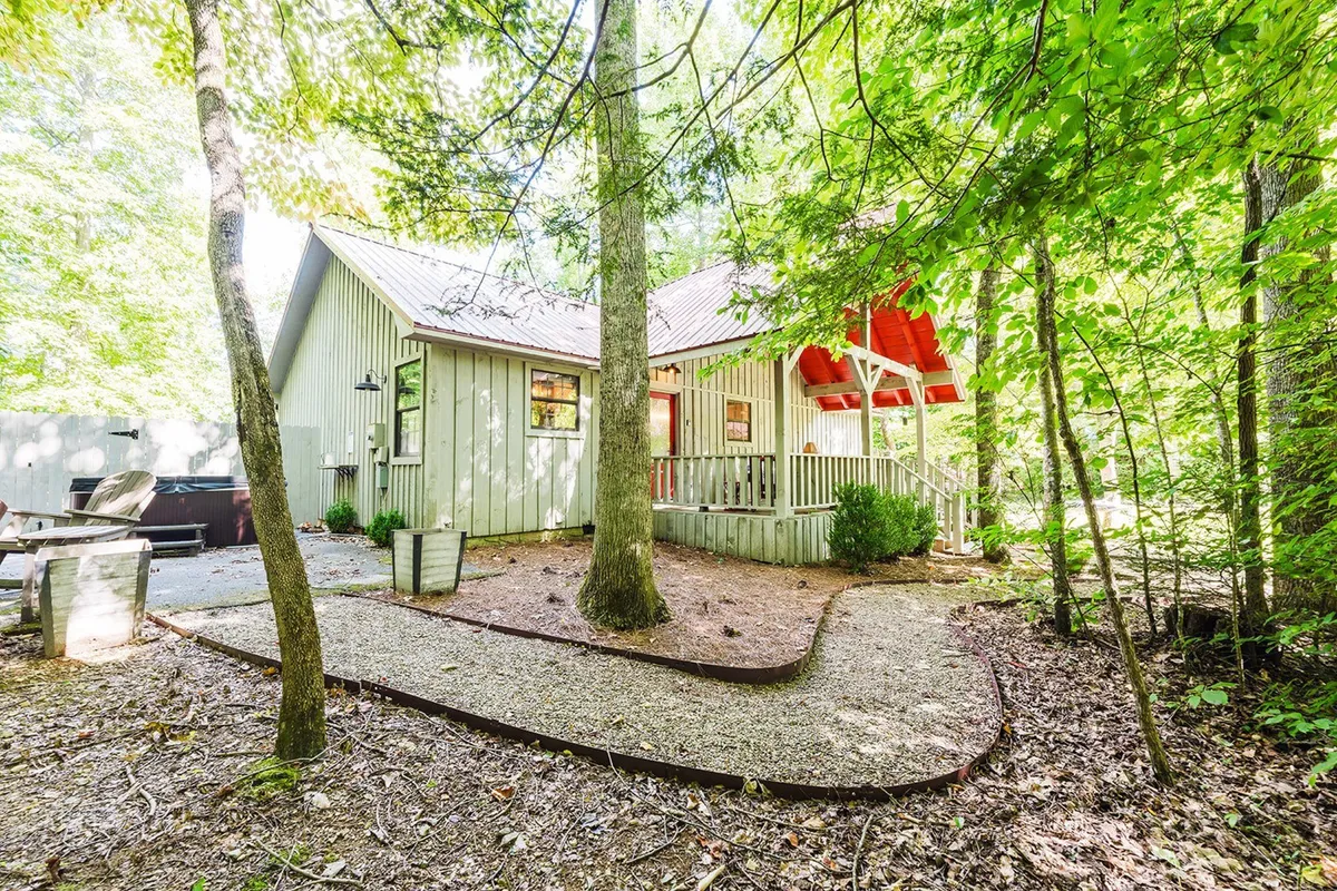 This image captures the charming exterior of the Summer Wind cabin, highlighting its vibrant red accents and lush greenery. The scene suggests a peaceful, semi-secluded yard perfect for relaxing with a pet or setting out on a nearby nature walk. The entrance and surroundings evoke a welcoming, pet-friendly atmosphere.