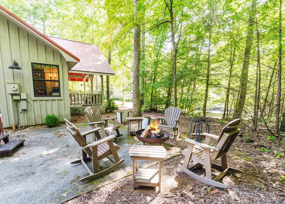 This image features a cozy outdoor fire pit area surrounded by Adirondack chairs, with the rustic cabin exterior and lush trees in the background. The setting exudes a sense of communal gathering, warmth, and connection to the surrounding nature—ideal for evening s’mores and storytelling under the stars.