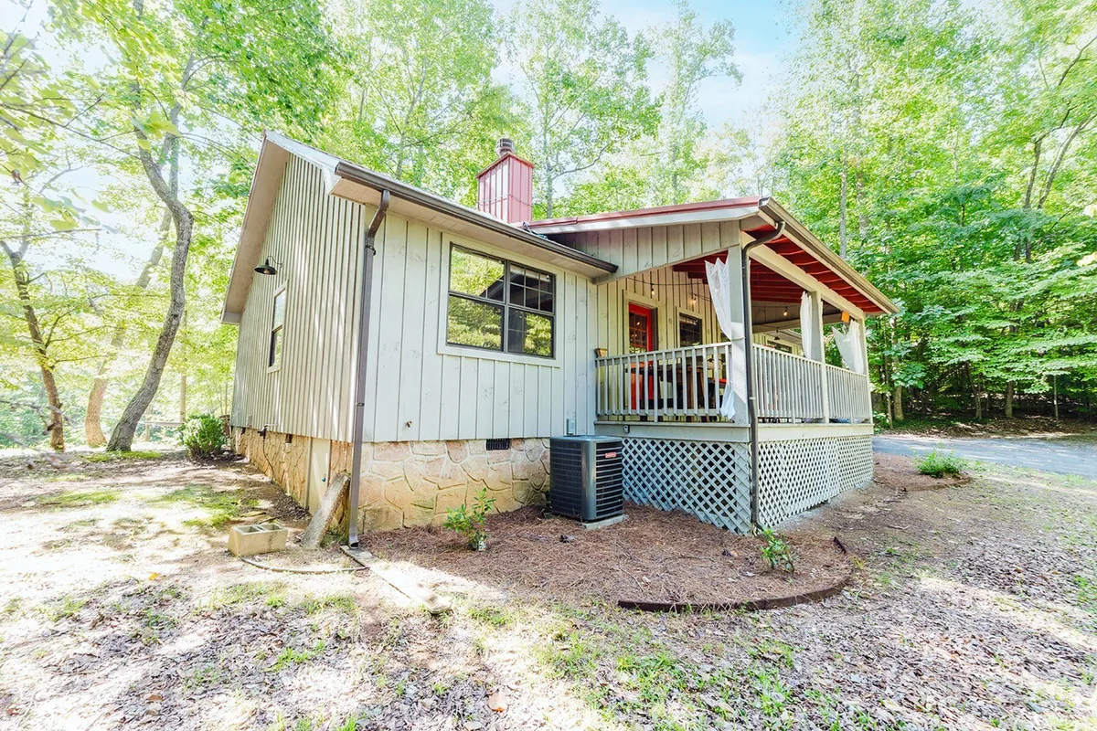 A welcoming exterior shot of a spacious wooden porch surrounded by trees, with comfortable seating and a peaceful atmosphere. The expansive porch hints at morning yoga sessions, leisurely breakfasts, and evenings spent watching sunsets or stargazing.