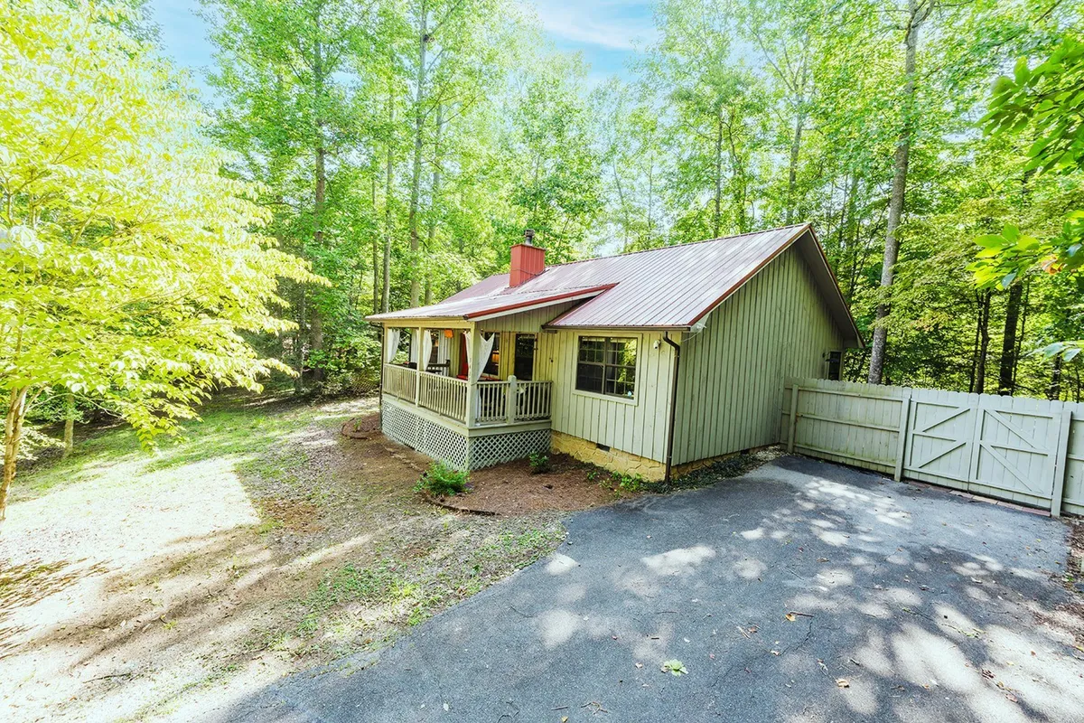 This image features the cabin’s exterior with a wooden porch under a red roof, surrounded by lush greenery. The porch invites guests to relax and enjoy the tranquil setting, while the expansive yard offers space for outdoor activities and gatherings.